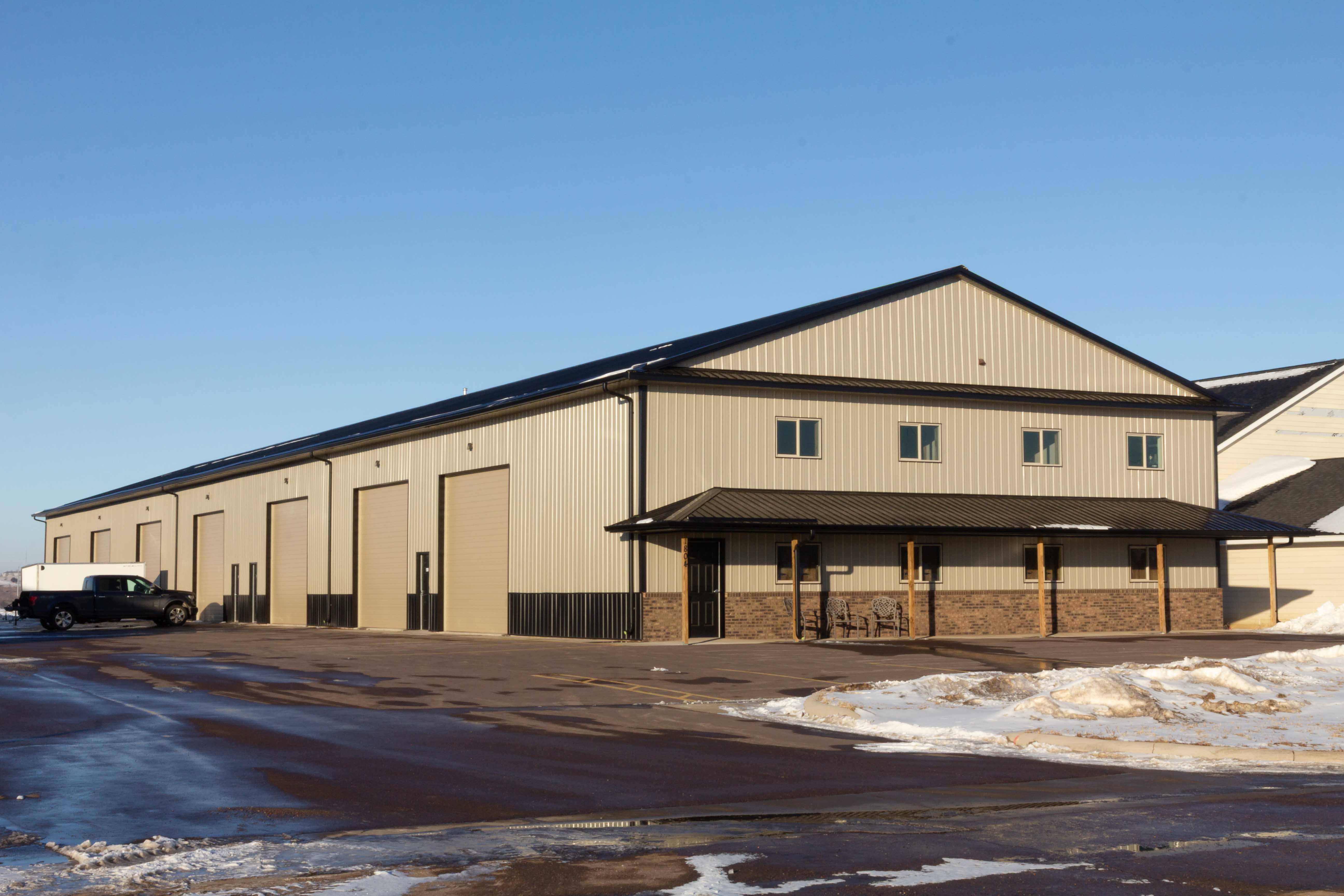 Two-story tan steel shop condo with a row of overhead doors, stone wainscot and a covered entry porch