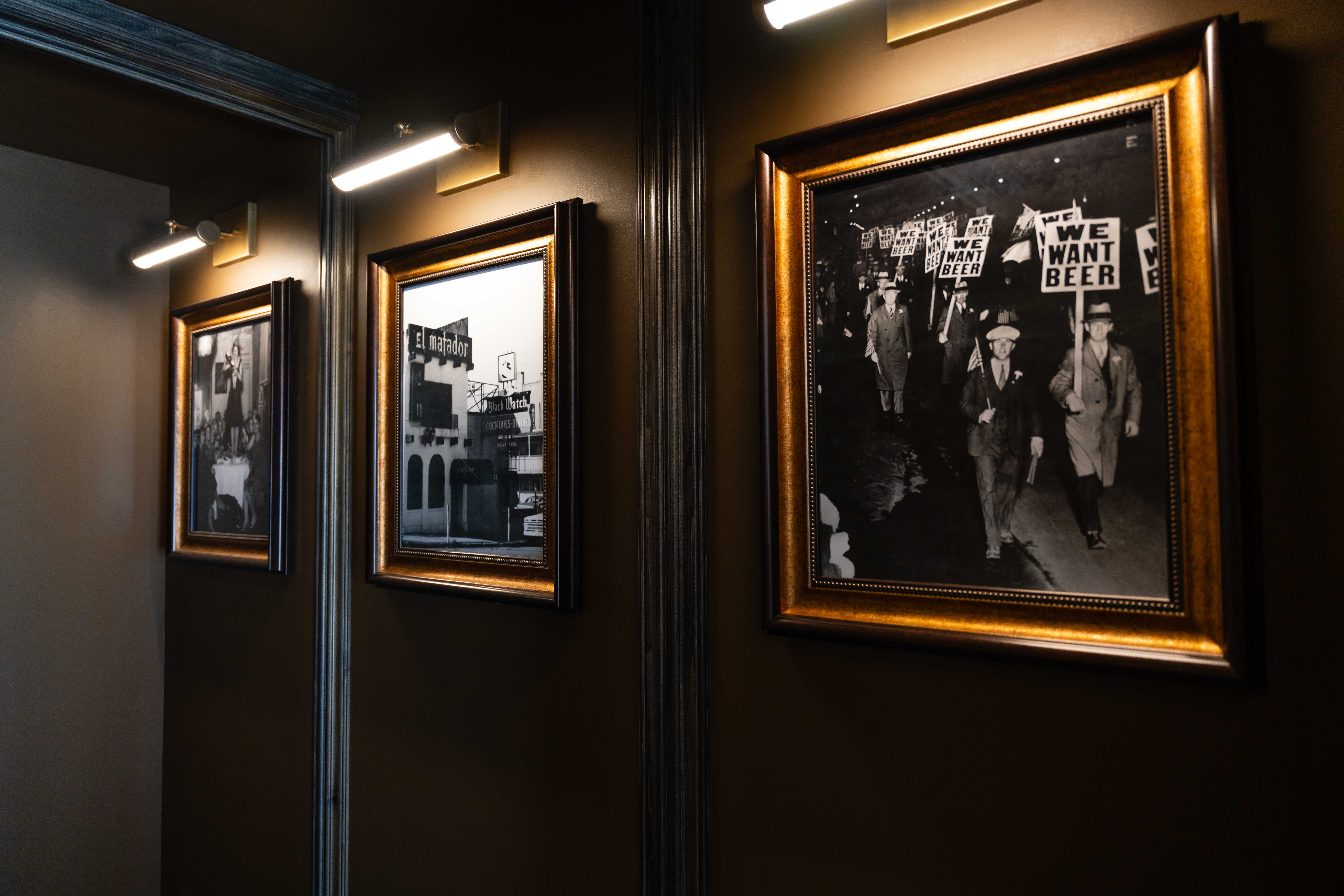 Dark hallway lined with gold-framed black-and-white historic photos lit by brass picture lights