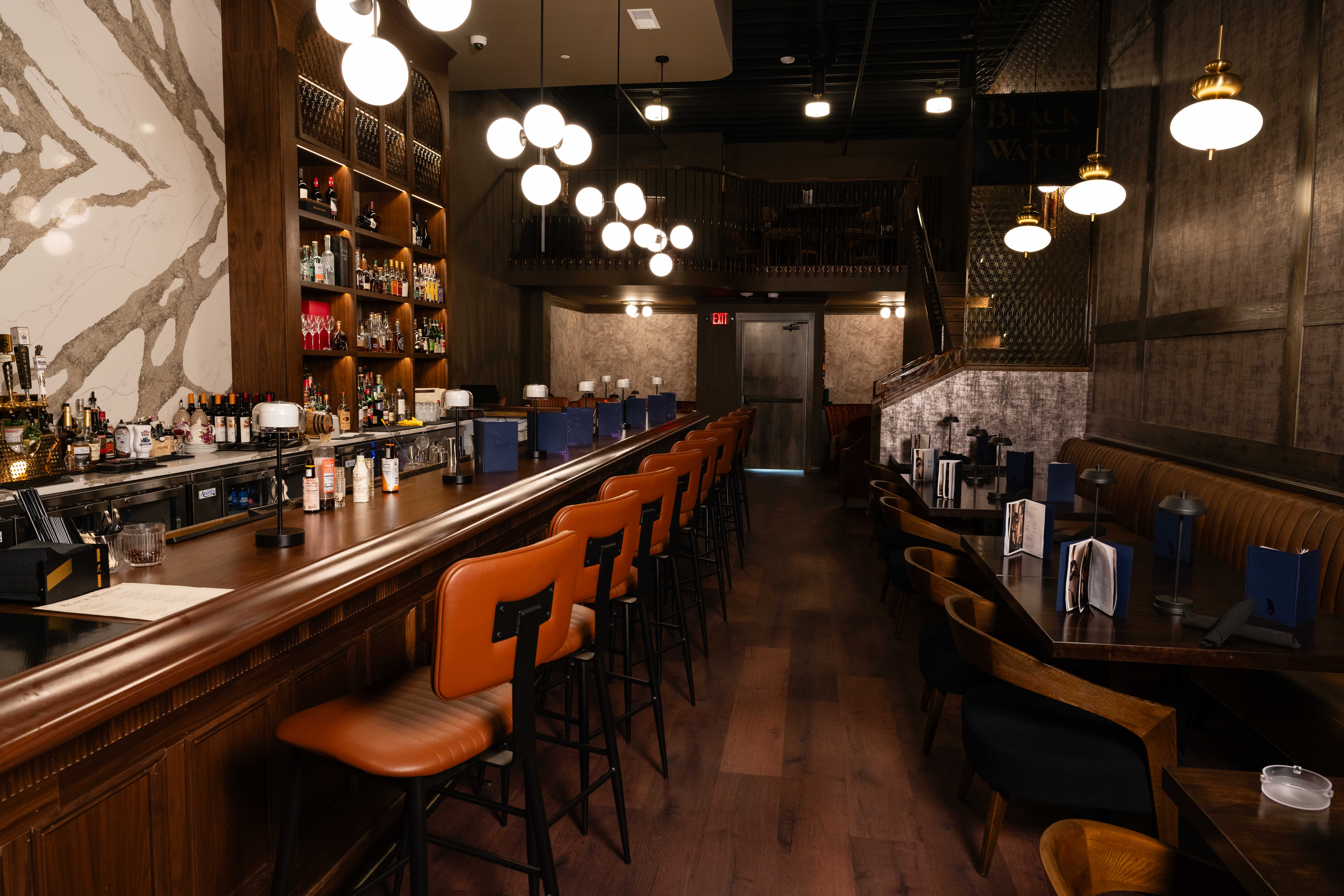 Speakeasy bar with leather stools, globe chandeliers and booth seating along textured walls in Sioux Falls, SD