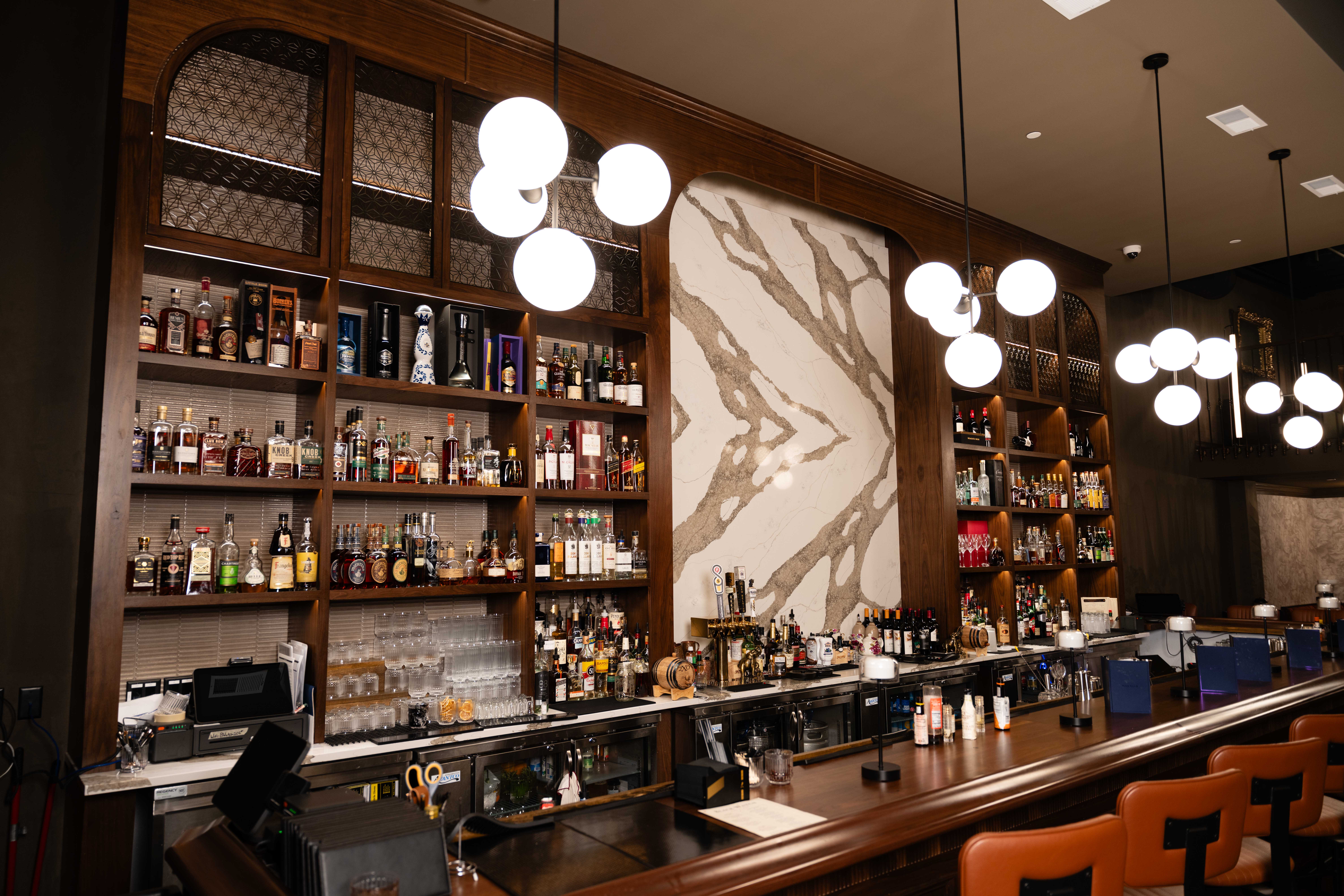 Back bar with walnut shelves of liquor bottles, a marble feature panel and globe pendant lights over the bar