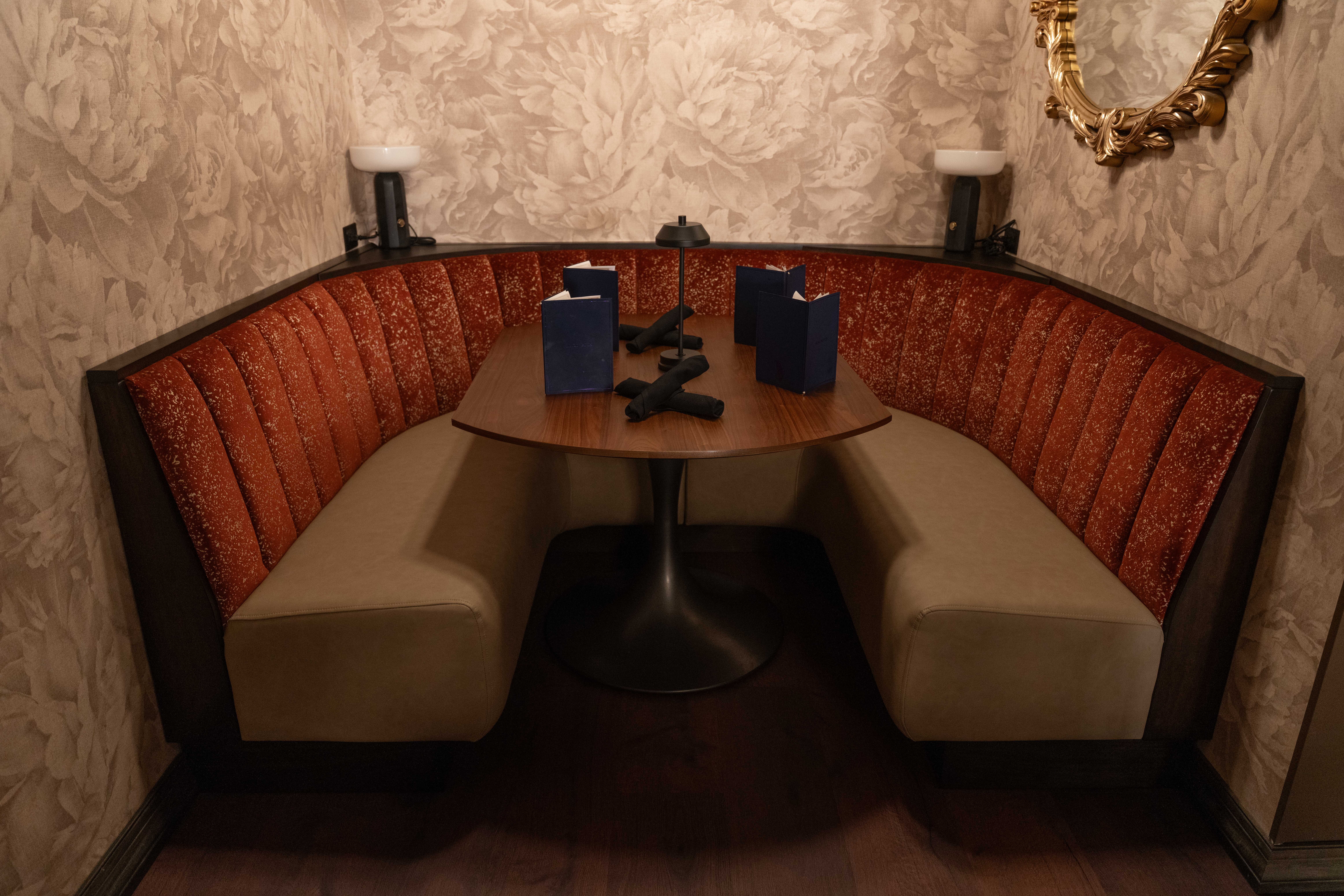 Curved rust velvet booth with a round pedestal table, navy menus and floral wallpaper at The Black Watch