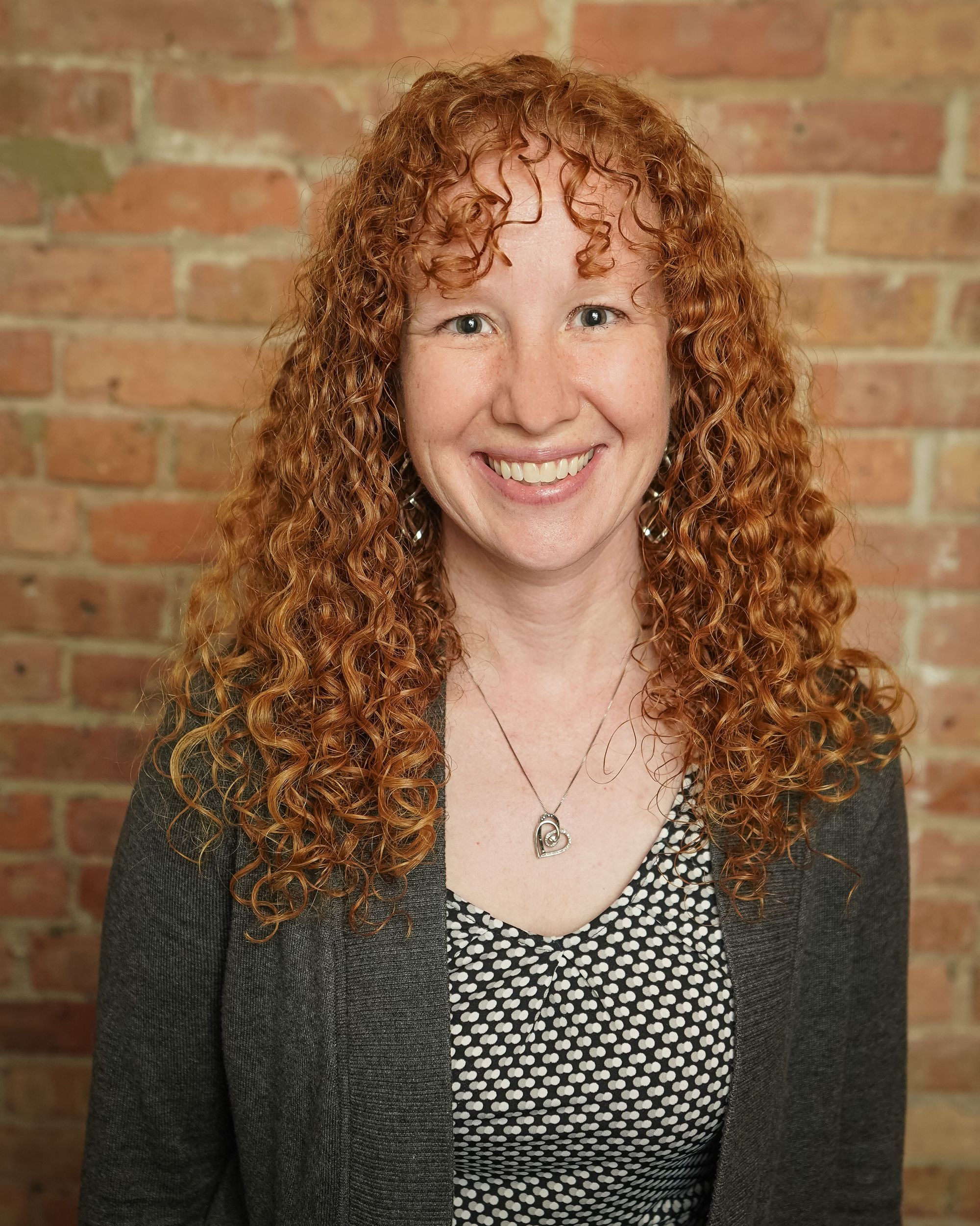 Elizabeth Herman smiling in a gray cardigan against a brick wall, telehealth-only counselor at Grow Wellness Group