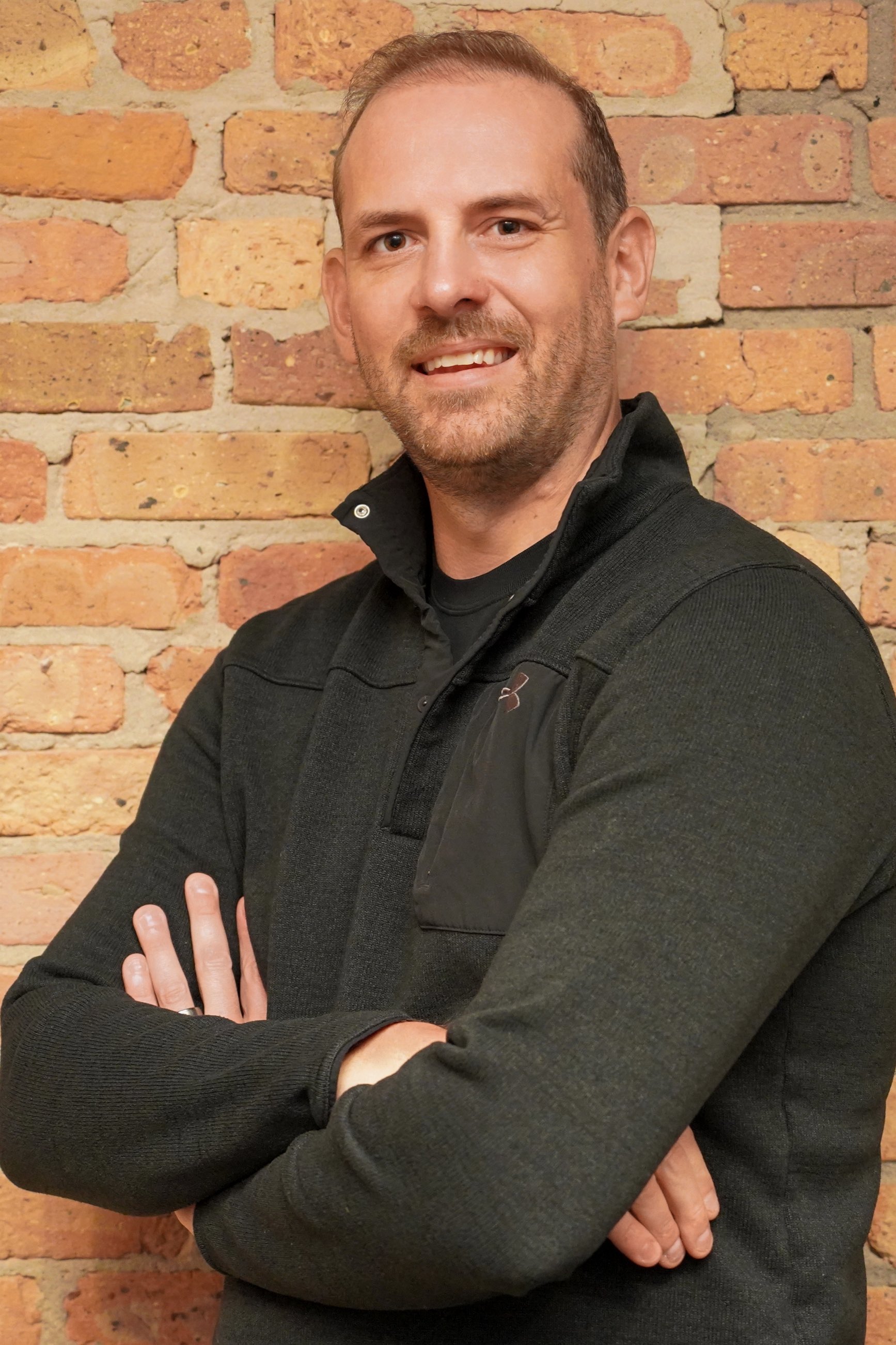 Jason Sandberg with arms crossed against a brick wall, telehealth counselor and sport consultant at Grow Wellness Group
