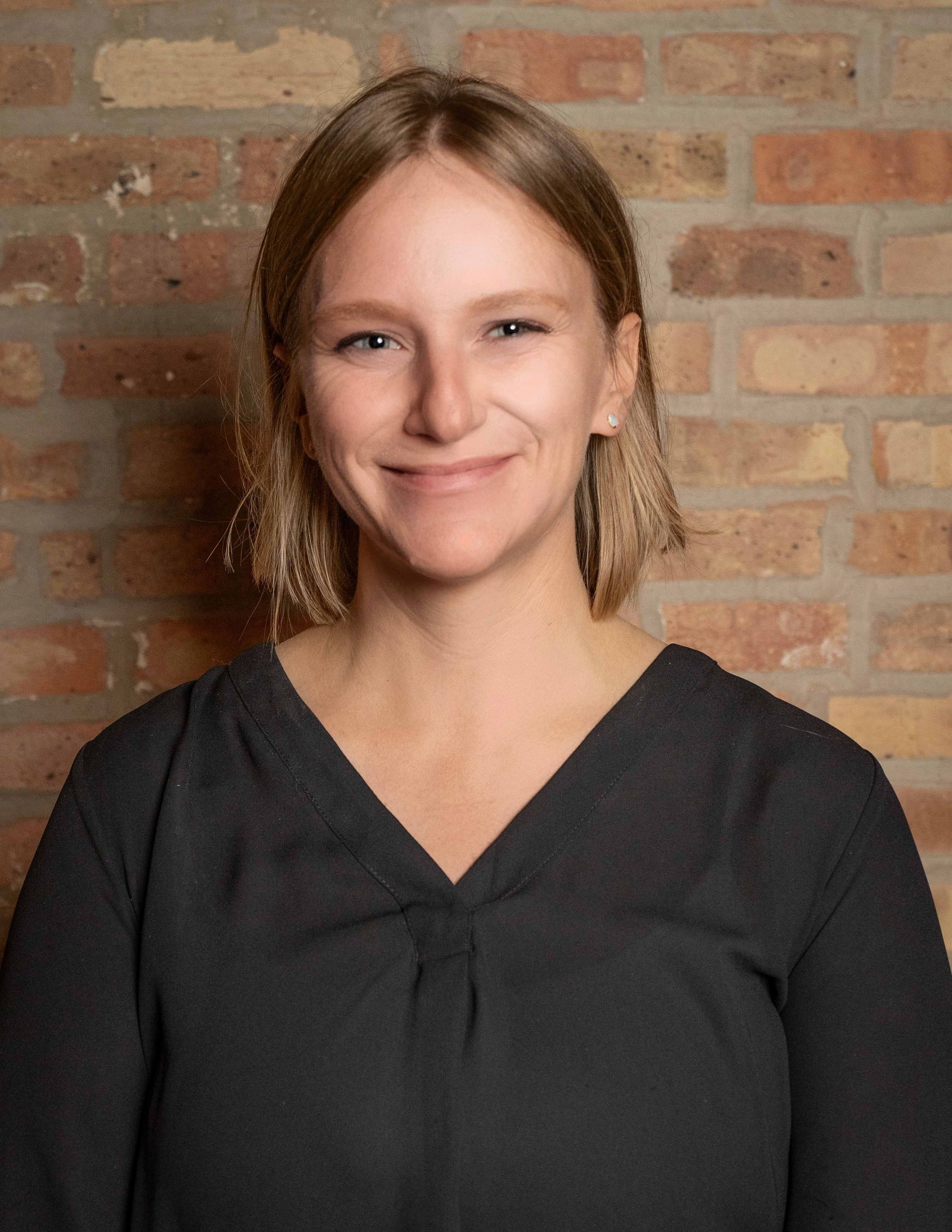 Kate Waller smiling against a brick wall, online therapist for adults, couples, and athletes at Grow Wellness Group