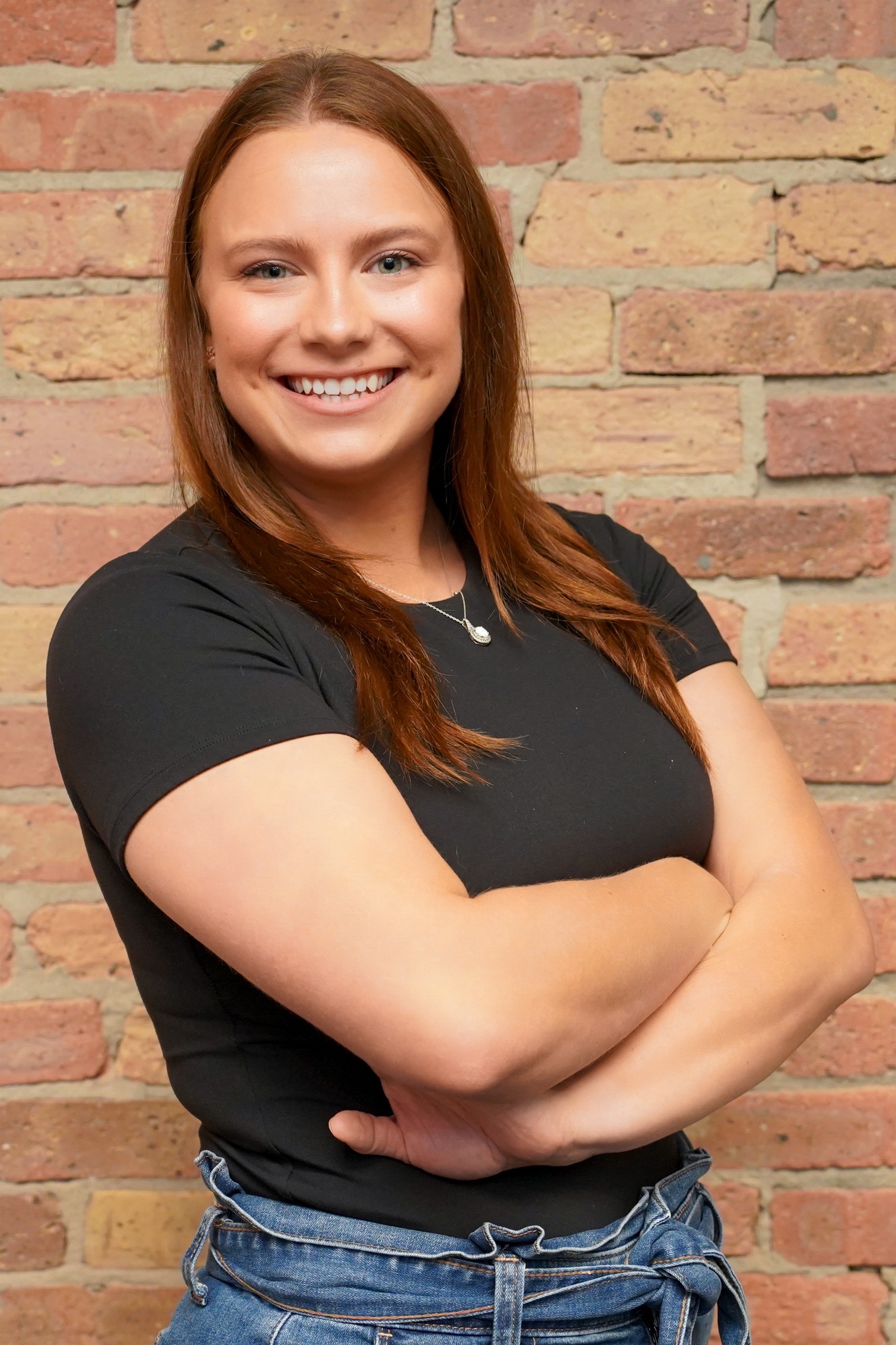 Julie Lown smiling with arms crossed against a brick wall, child and adolescent teletherapy counselor at Grow Wellness Group