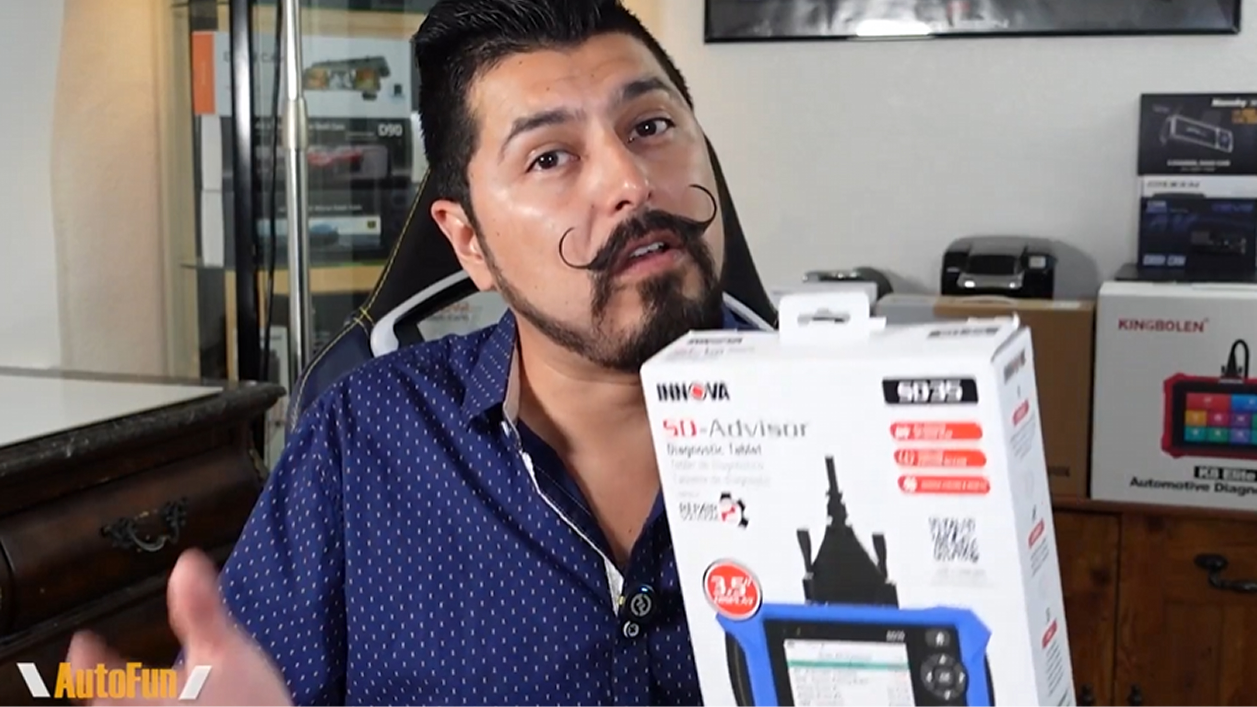 Man with styled mustache and beard holding an Innova SD-Advisor diagnostic tablet box in a room with automotive diagnostic products.