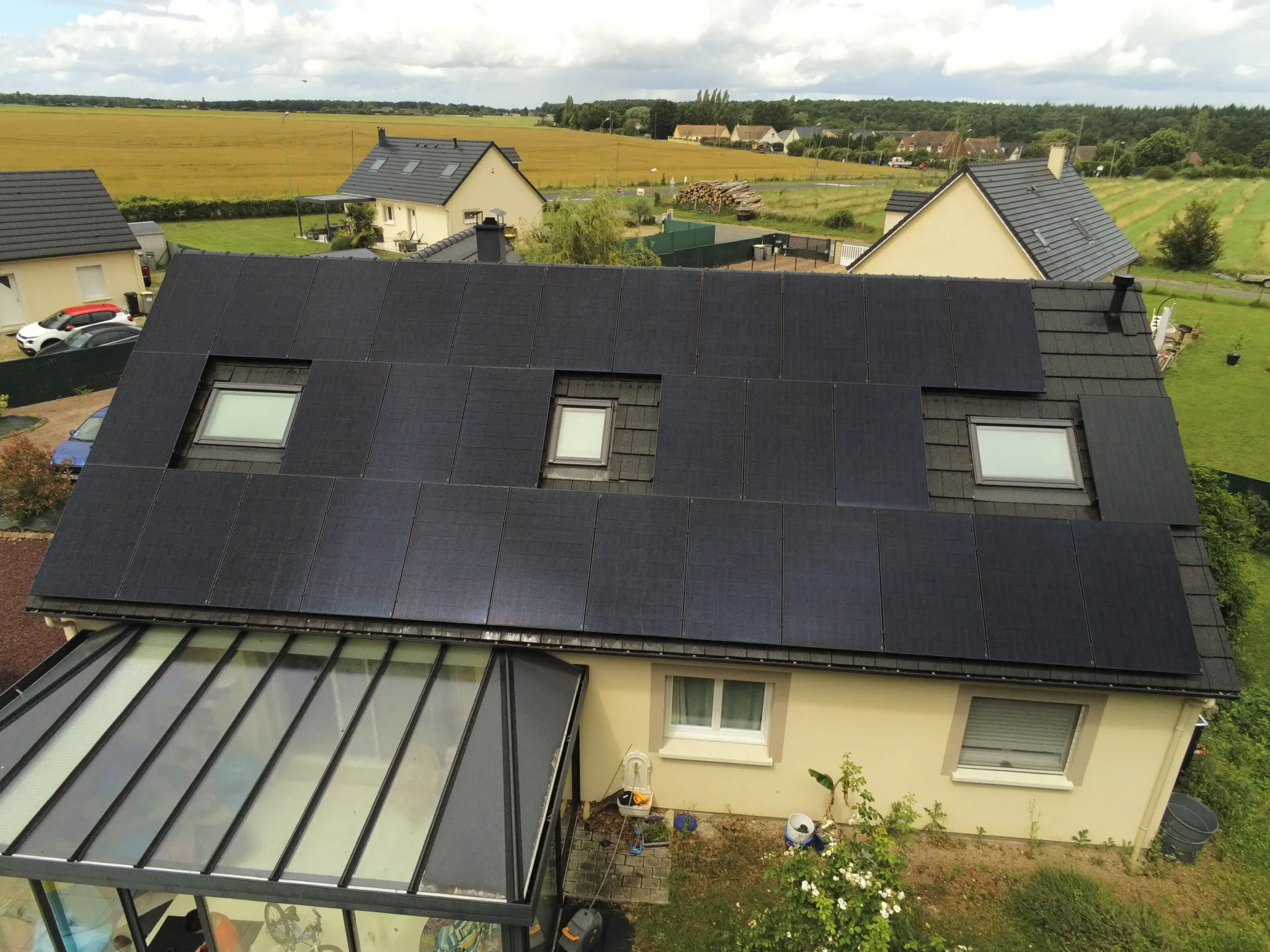 Vue en hauteur de la maison, son pan de toiture couvert de modules entre les fenêtres de toit, à Fontaine-sous-Jouy (27120)