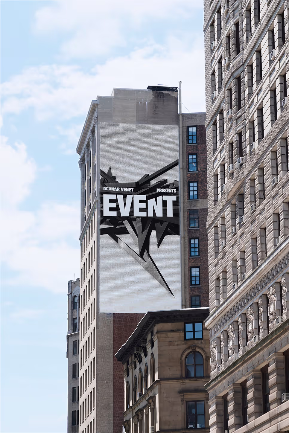 Tall city buildings with a large mural saying 'EVENT' on a white brick wall under a partly cloudy sky.