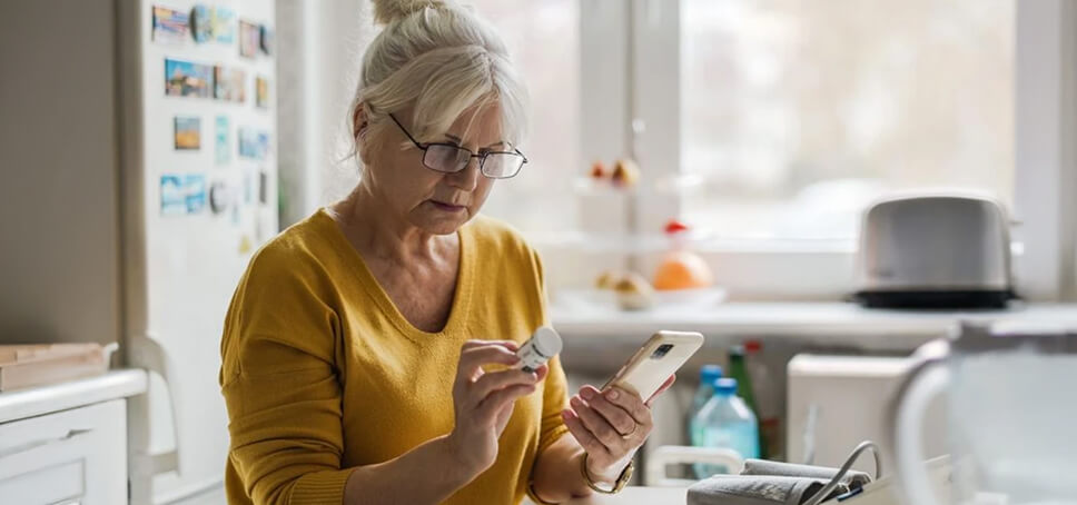 White haired woman wearing yellow shirt looks at a medication bottle