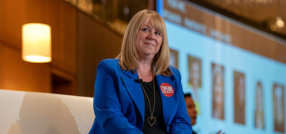 Woman wearing blue blazer sits on a couch on stage.