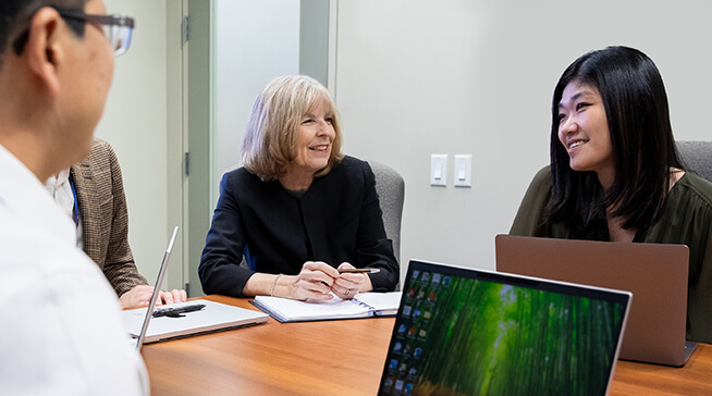 Dr. Paula Rochon, Director of Research at the Weston and O’Born Centre for Mature Women’s Health and Joyce Li, the Centre’s Research Manager, seated in a brightly lit boardroom, engaging in conversation near an open laptop.