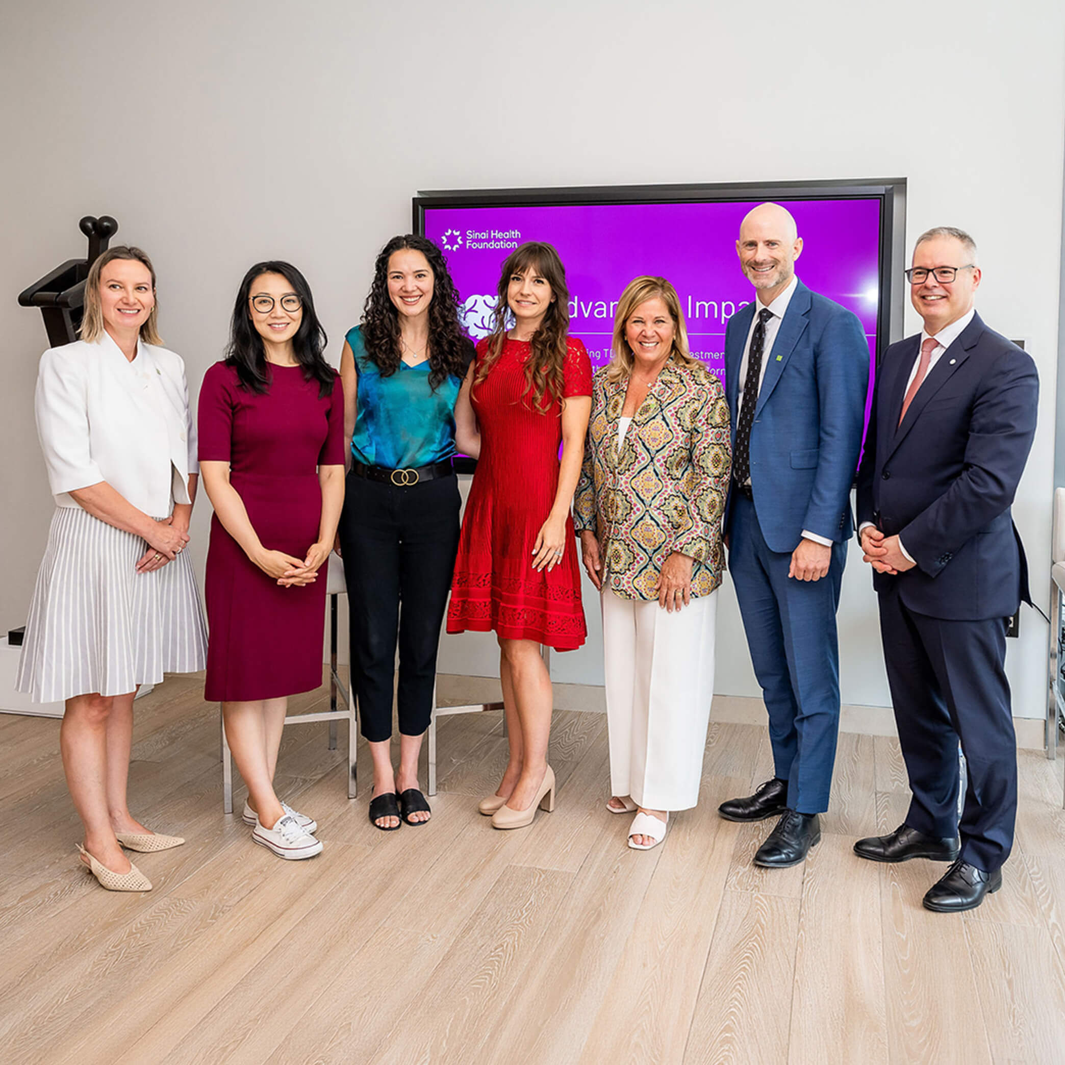 Group of people stand smiling in front of a purple background