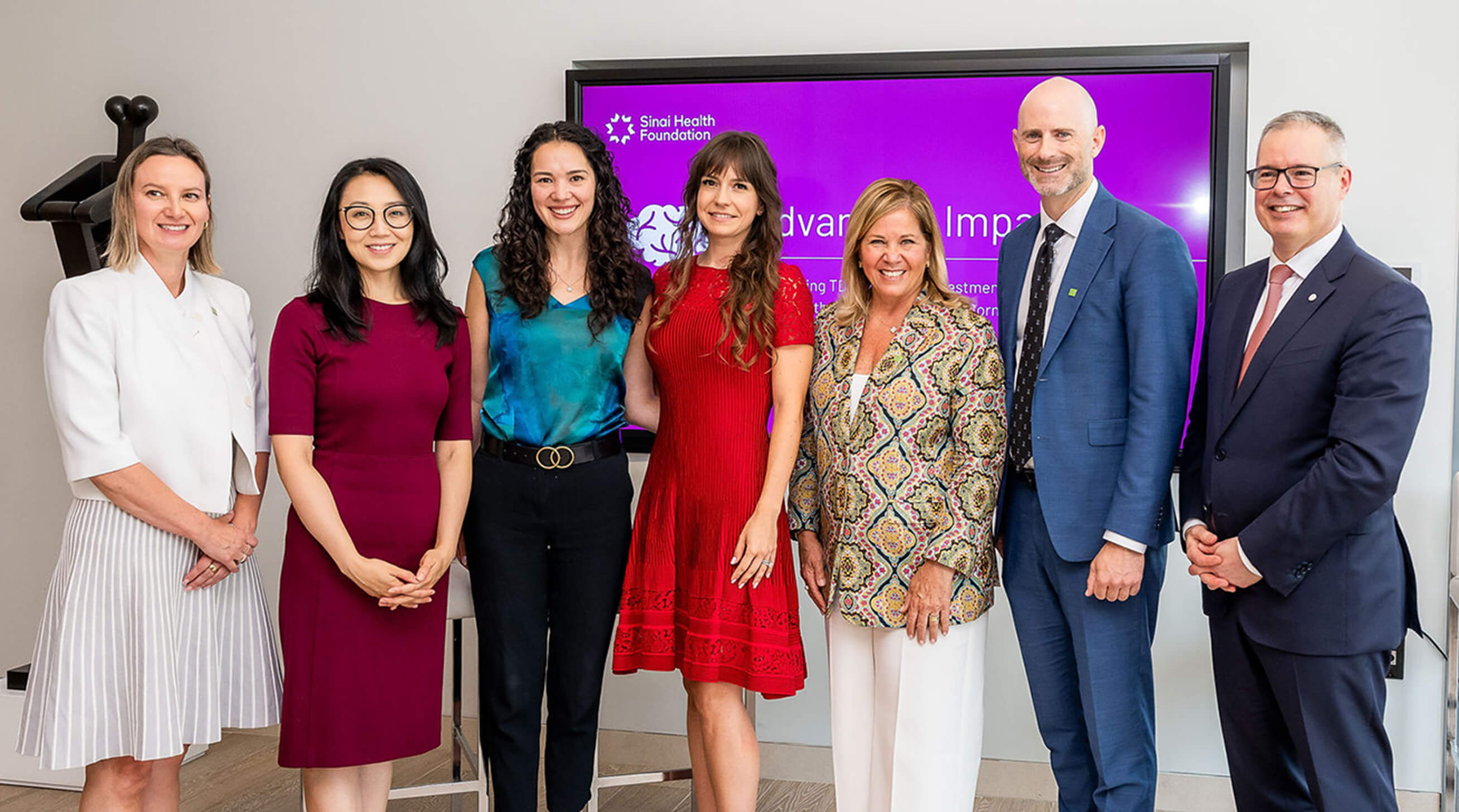 Group of people stand smiling in front of a purple background