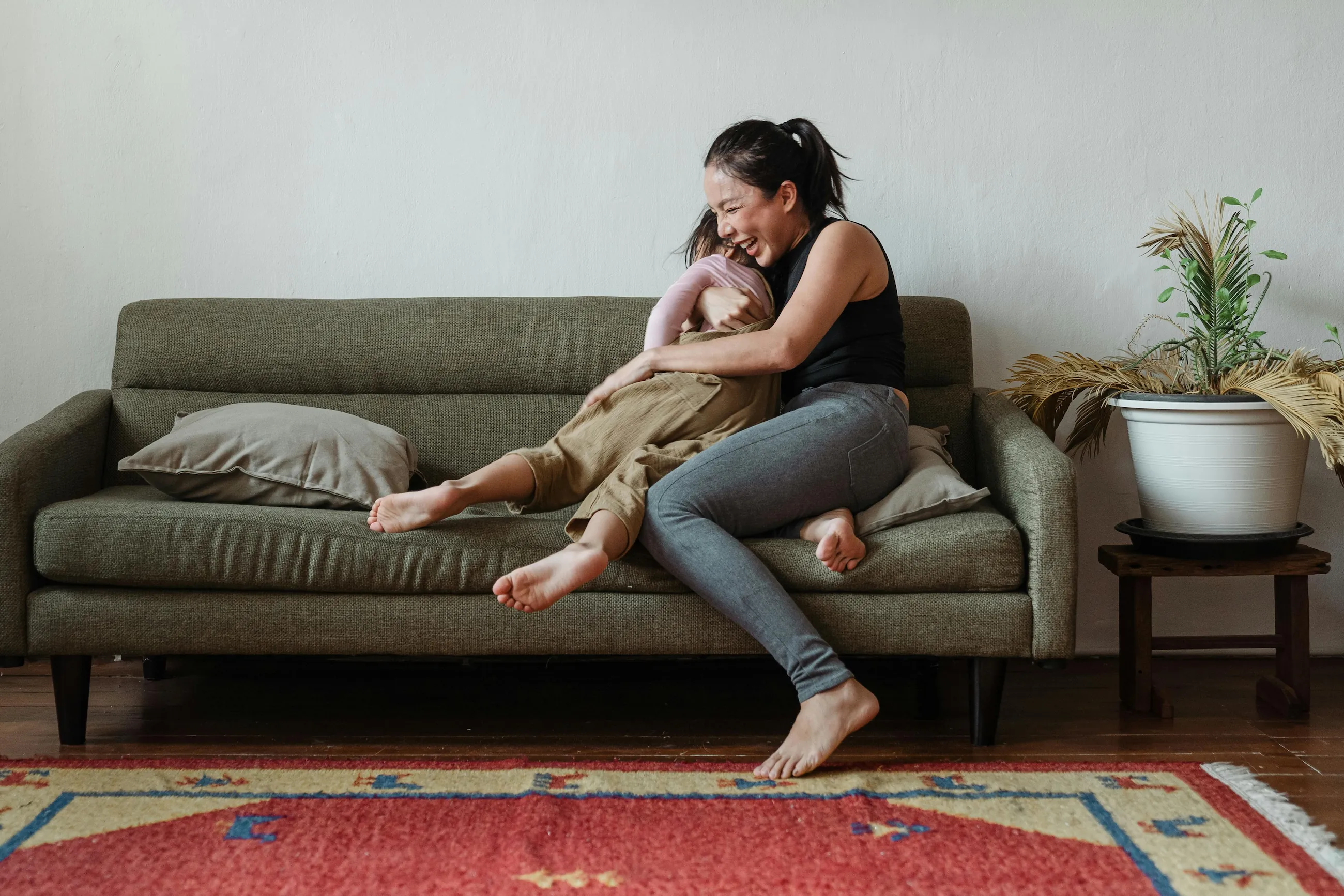 Smiling mother playfully lifting her child on a sofa at home