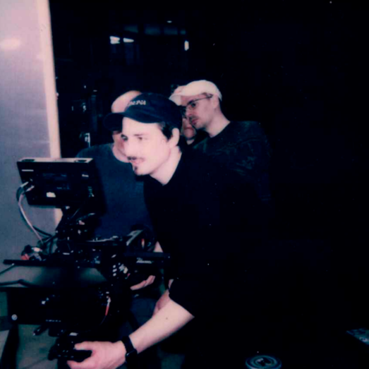 Drei Männer bei einer Filmproduktion, einer bedient eine Kamera mit Monitor.