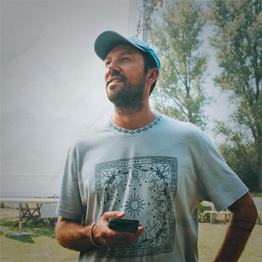 Junge Frau mit hochgestecktem Haar und hellem, mit Reißverschluss versehenem Pullover sitzt lächelnd an einem Tisch in einem hellen Raum.
