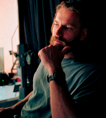 Schwarz-weiß-Porträt eines Mannes mit Bart und zurückgebundenen Haaren, der ernst in die Kamera blickt