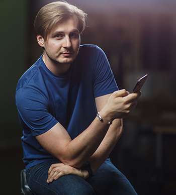 Schwarz-weiß-Porträt eines lächelnden jungen Mannes mit zurückgekämmten Haaren, aufgenommen im Freien mit unscharfem Hintergrund.