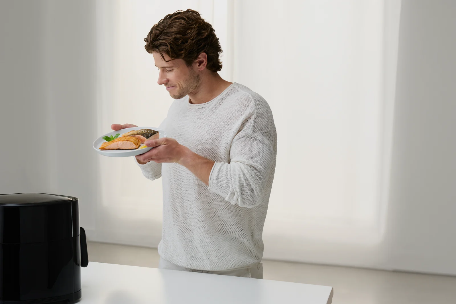 Mann serviert Lachs aus dem SEVERIN AI-Fryer in einer hellen Küche