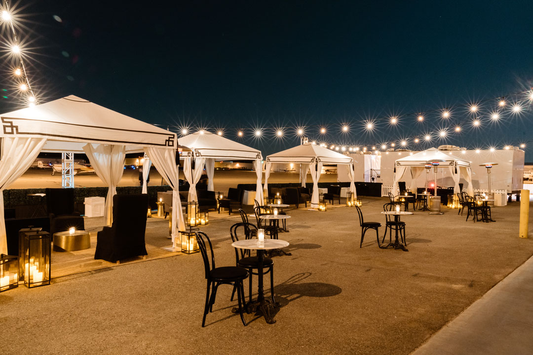 White cabanas, string lights and bistro tables set up on the tarmac outside The Executive Hangar at night