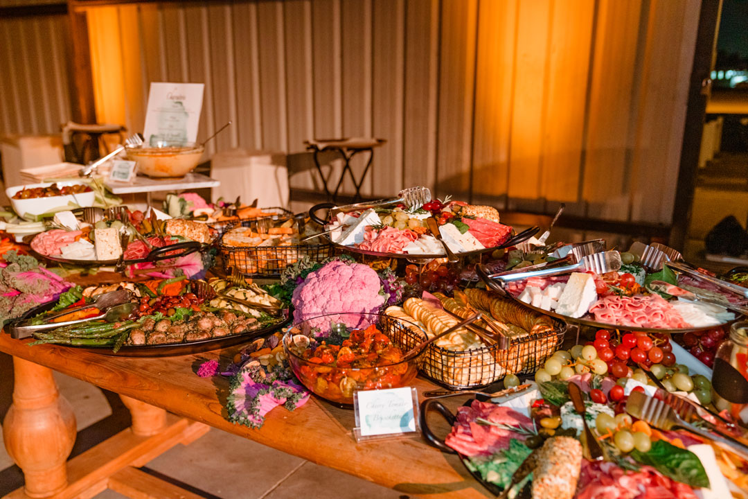 Charcuterie and crudite station on a wood farm table with cured meats, cheeses, crackers, grapes and purple cauliflower