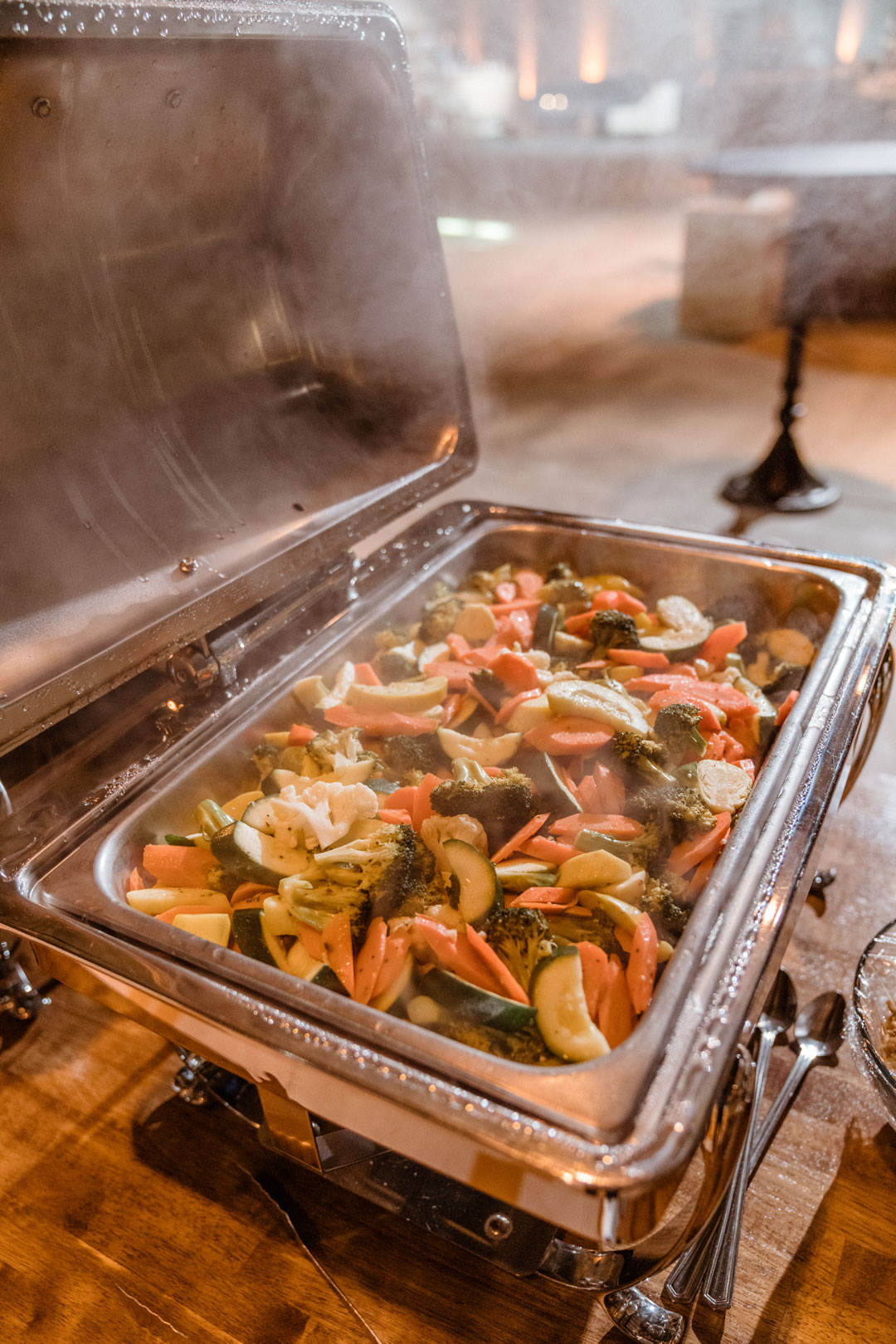 Steaming chafing dish of vegetable medley with zucchini, carrots, broccoli and cauliflower on the wood buffet