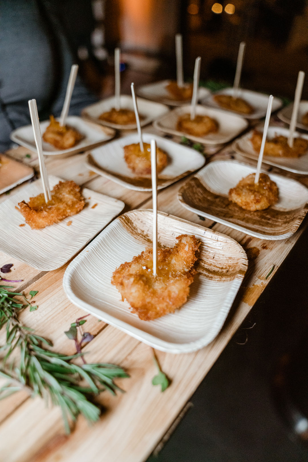 Coconut crusted shrimp on skewers served in small palm leaf plates with fresh rosemary sprigs
