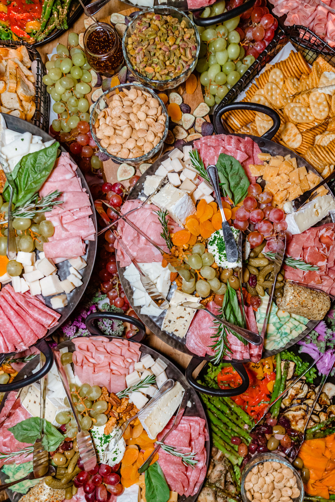 Overhead view of charcuterie platters with salami, prosciutto, cheese wedges, grapes, dried apricots, nuts and crackers