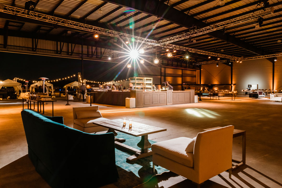 Teal velvet sofa and cream armchairs around a wood coffee table facing the central bar inside The Executive Hangar