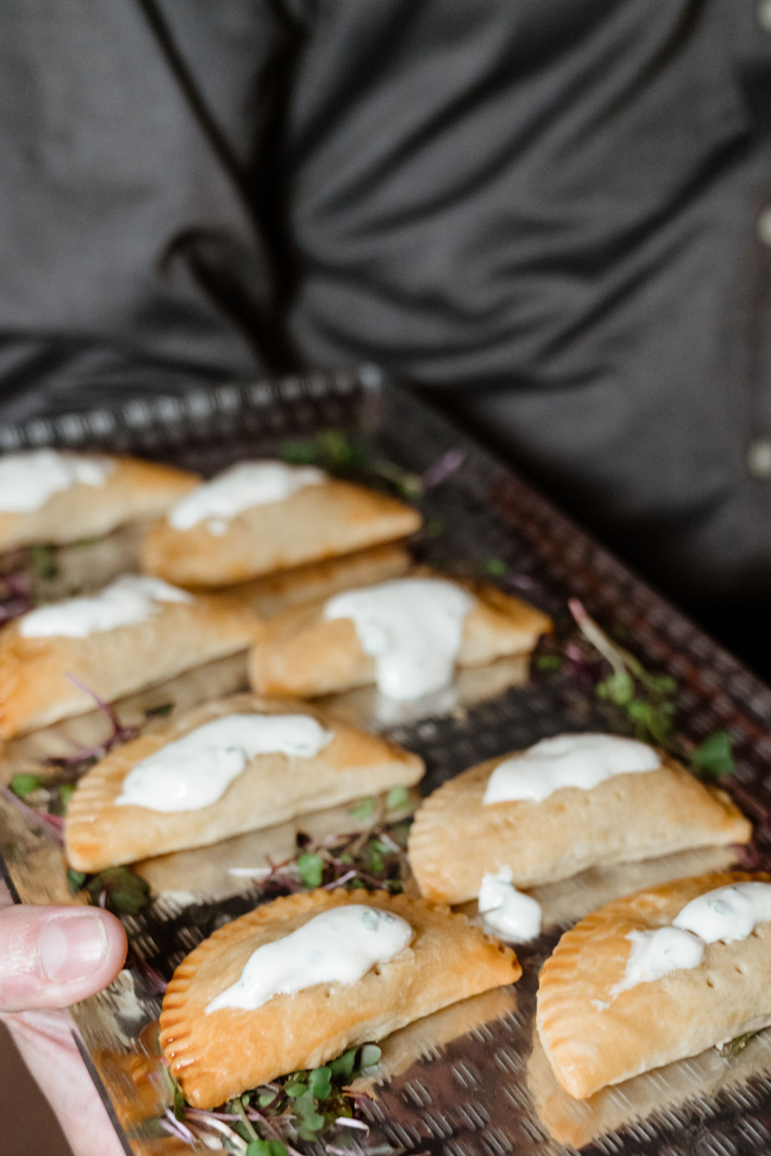 Server holding a tray of chicken jalapeno empanadas topped with cream sauce over microgreens