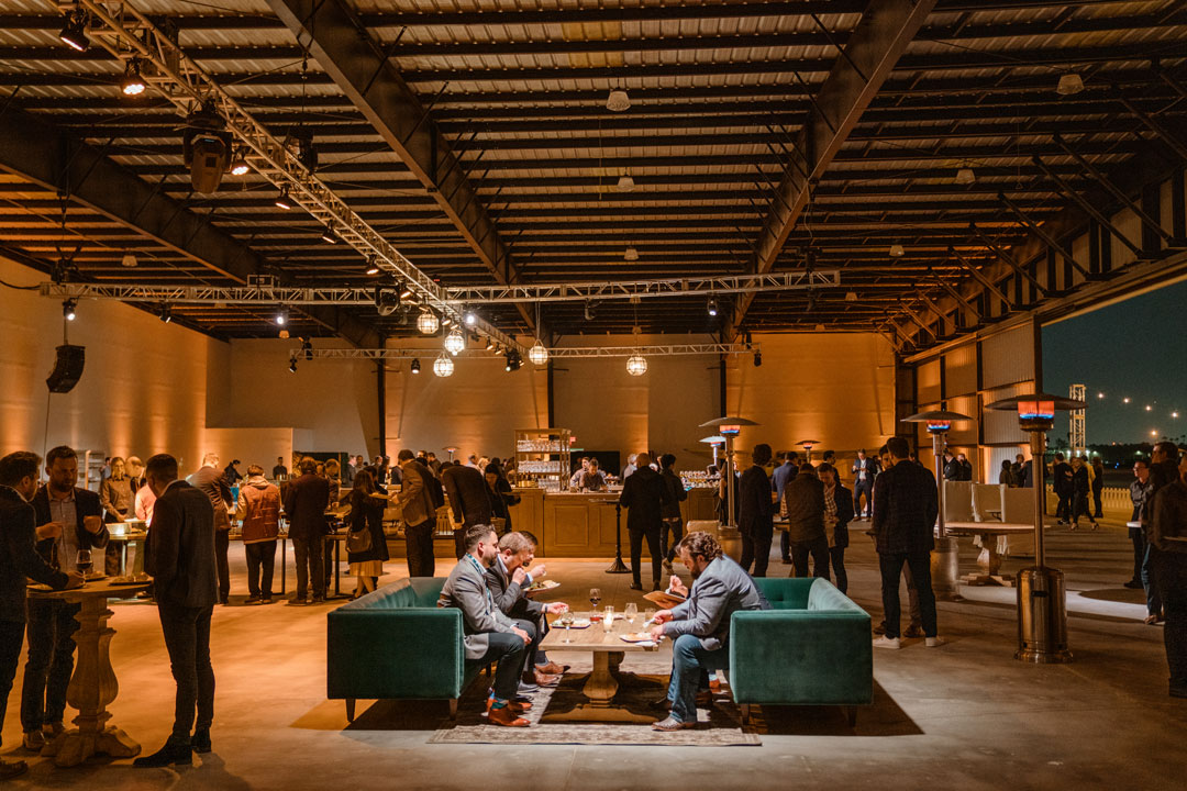 Guests eating on green velvet sofas at the Zendesk corporate party, hangar door open to the night