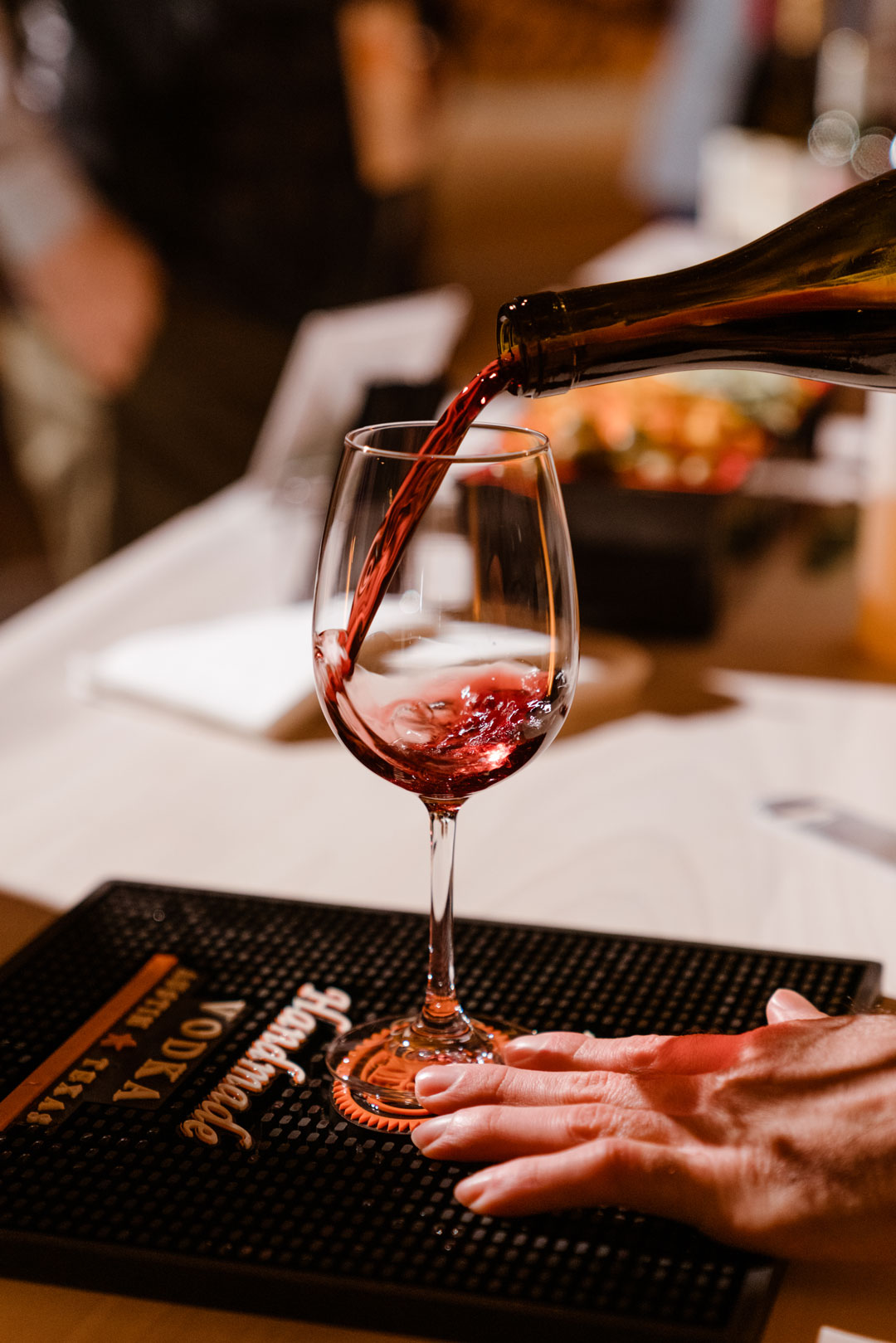Red wine poured into a single stemmed glass as a hand steadies it on a bar mat