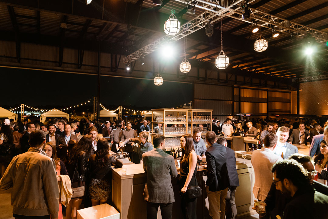 Guests crowd the central bar under lantern pendant lights at the Zendesk corporate party in the hangar