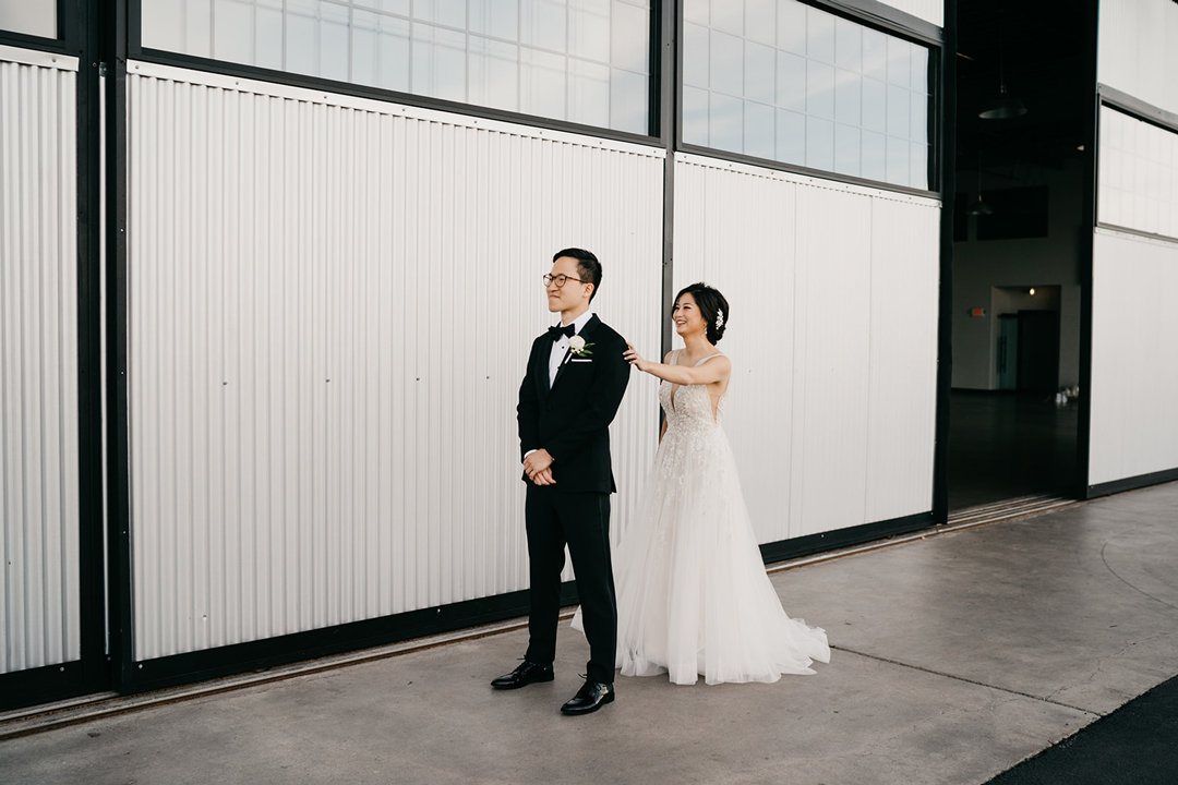 Kayla tapping Justin on the shoulder for their first look outside the white corrugated wall of Hangar 21 South