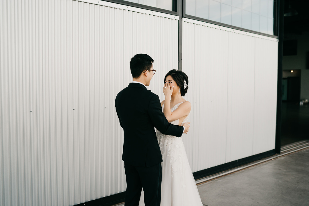 Justin holding Kayla as she wipes away tears during their first look outside Hangar 21 South