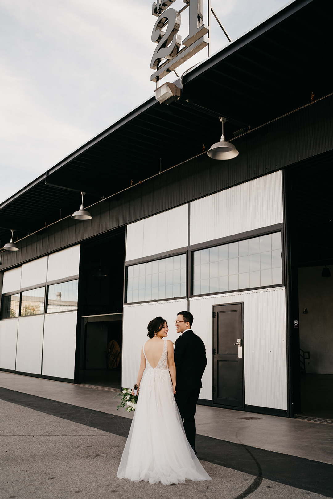 Kayla and Justin walking hand in hand toward the Hangar 21 entrance beneath the large 21 sign