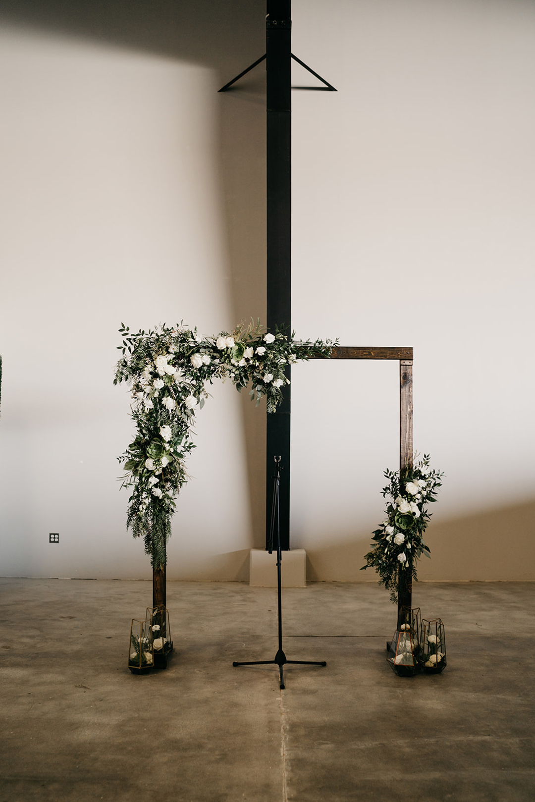 Wooden ceremony arbor draped with white flowers and greenery in the white-walled Executive Hangar