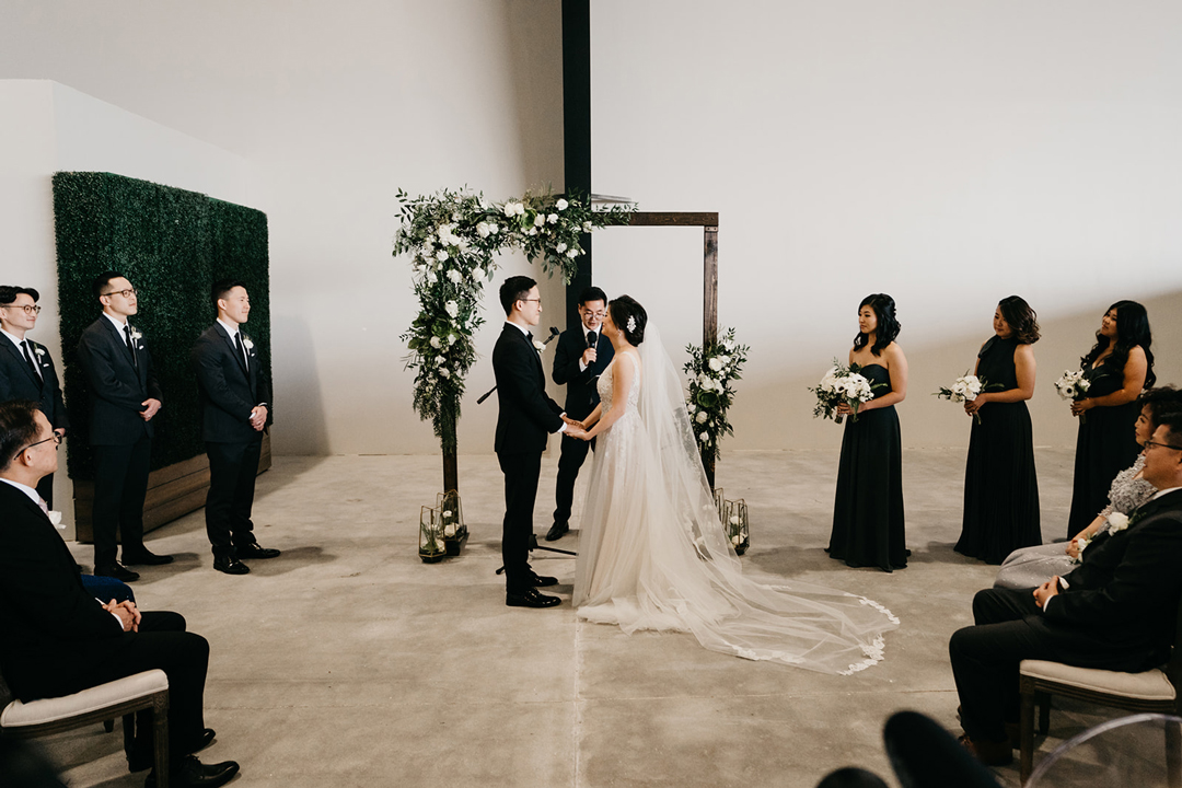 Kayla and Justin exchanging vows at the wooden arbor while bridesmaids in green and groomsmen stand beside them