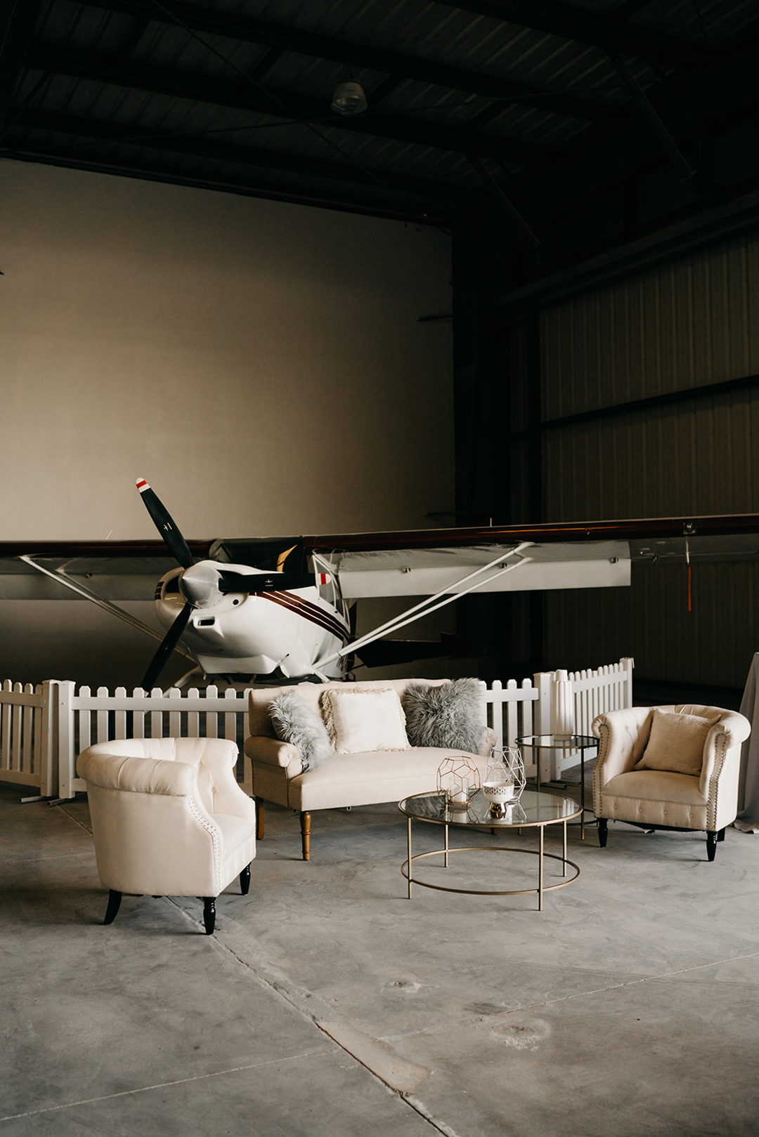 Cocktail hour lounge with tufted cream sofas and a gold coffee table set in front of a small propeller plane