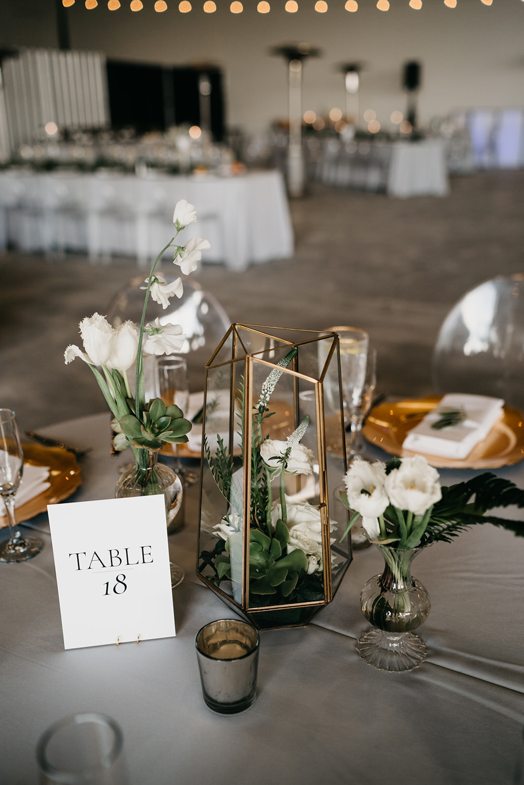 Table 18 centerpiece with a gold geometric terrarium, white tulips and greenery on grey linen