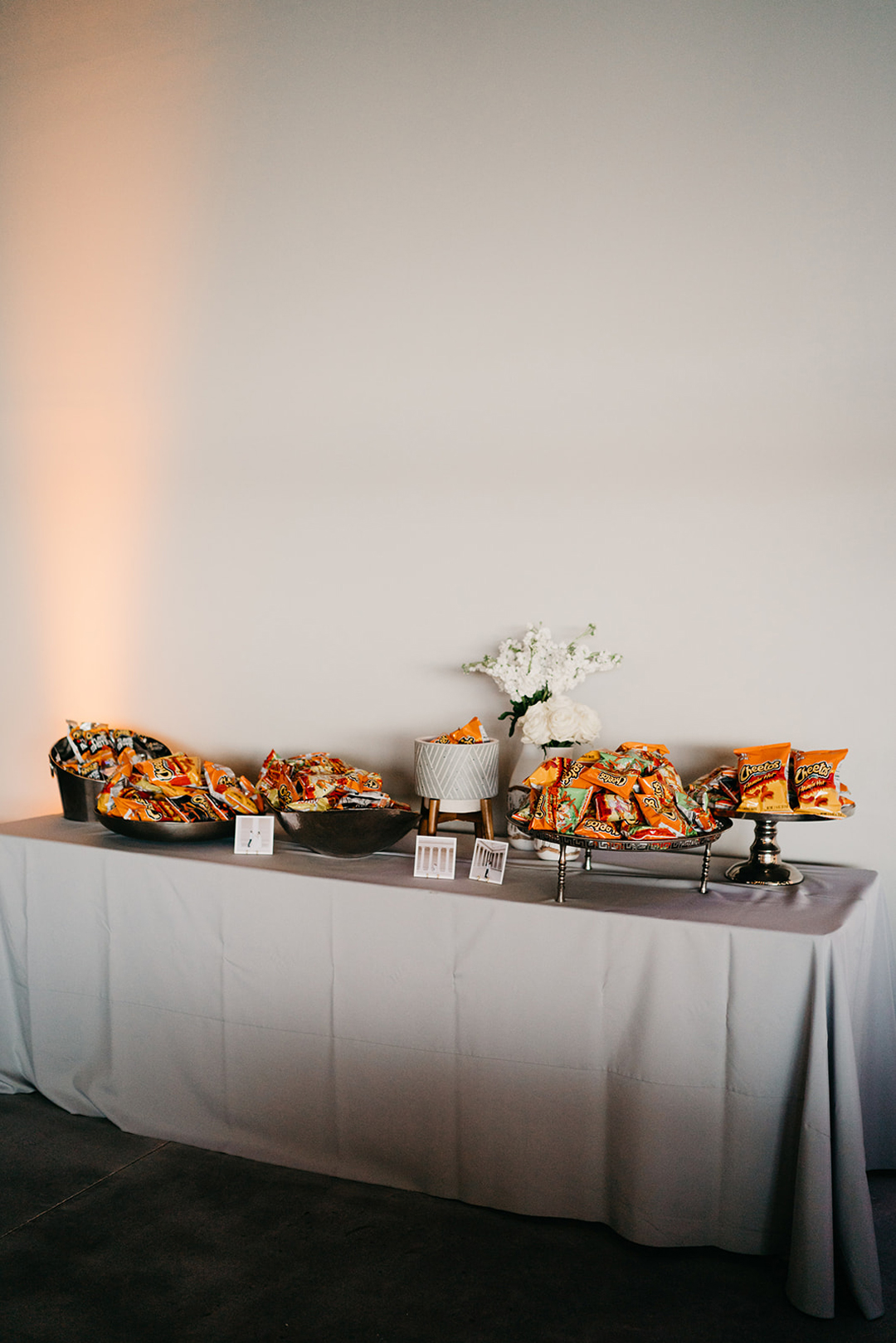 Snack table with bowls of chips and a white floral arrangement on grey linen at the reception