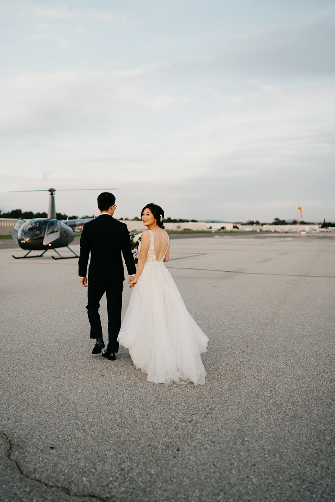 Kayla and Justin walking hand in hand across the tarmac toward a helicopter for their flight over Orange County