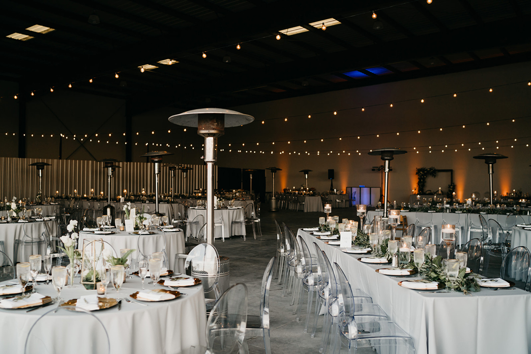 Reception tables with patio heaters, cafe lights and clear chairs filling the 28,000 square foot hangar