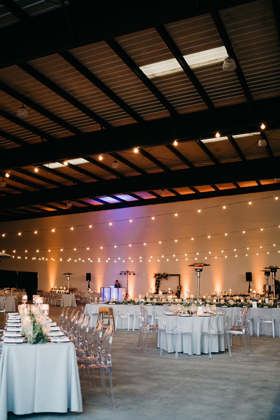 Wide view of the reception in The Executive Hangar with string lights, amber uplighting and set tables