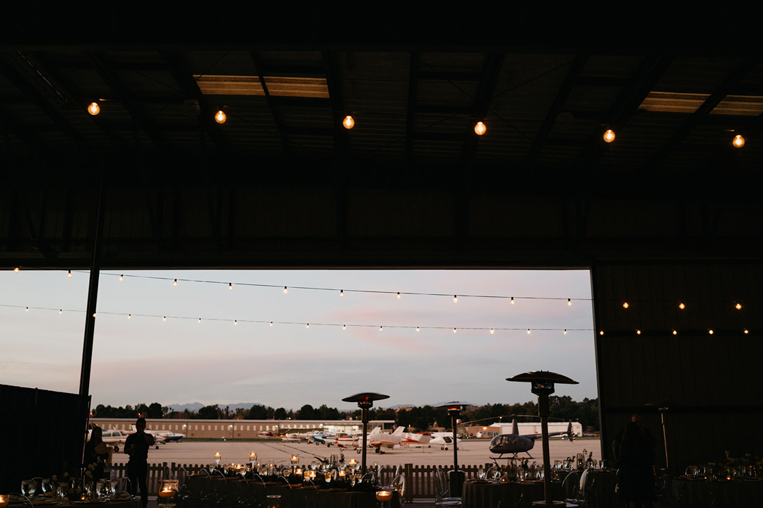 View from inside the hangar at dusk looking out over parked planes and a helicopter on the tarmac