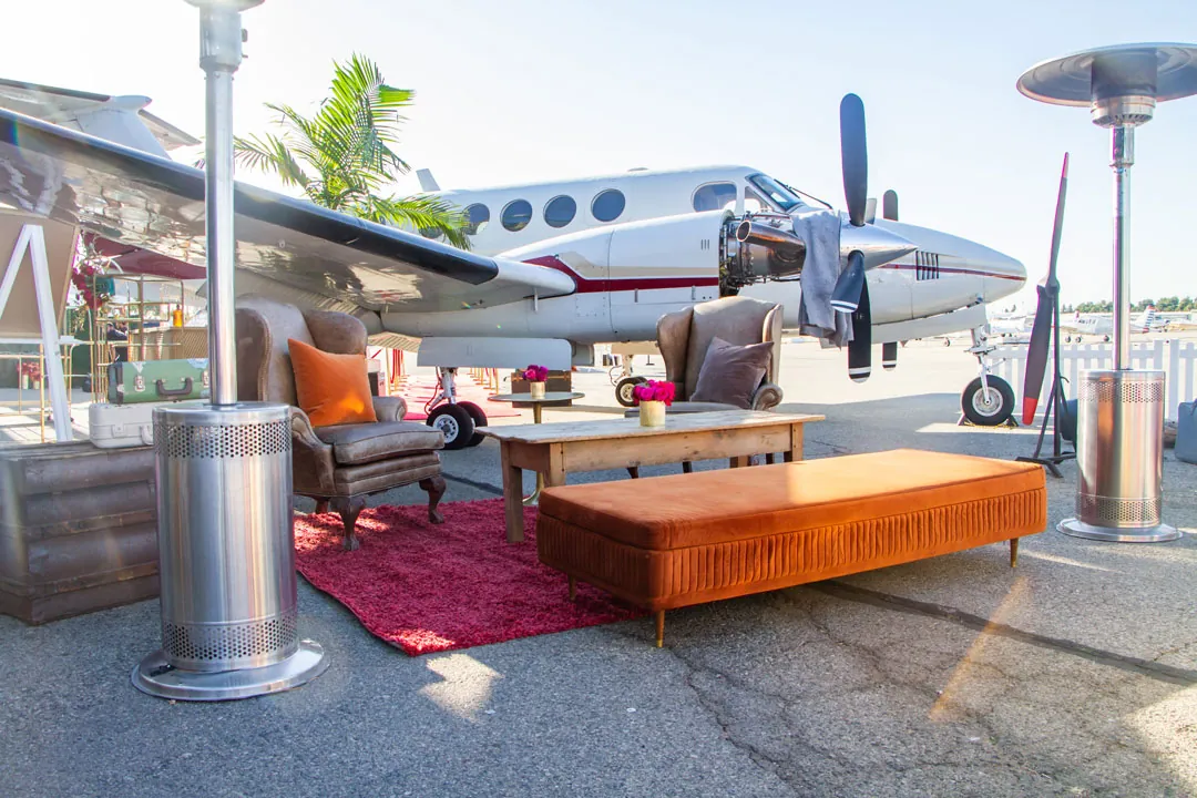 Leather armchairs, orange velvet bench and heat lamps form a lounge under a twin-engine plane at The Executive Hangar
