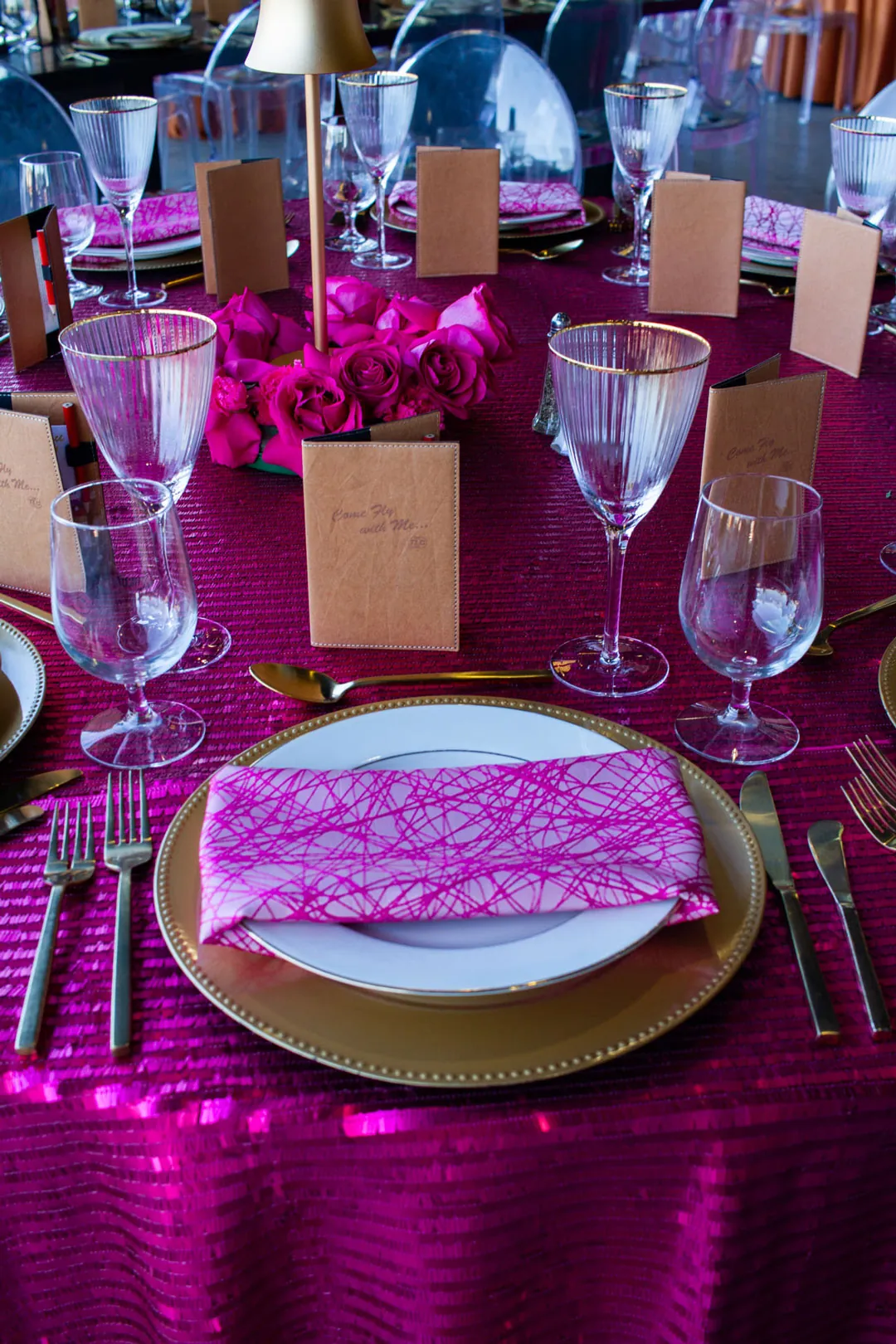 Fuchsia sequin table with gold chargers, pink patterned napkins, gold-rimmed glassware and pink roses at the gala
