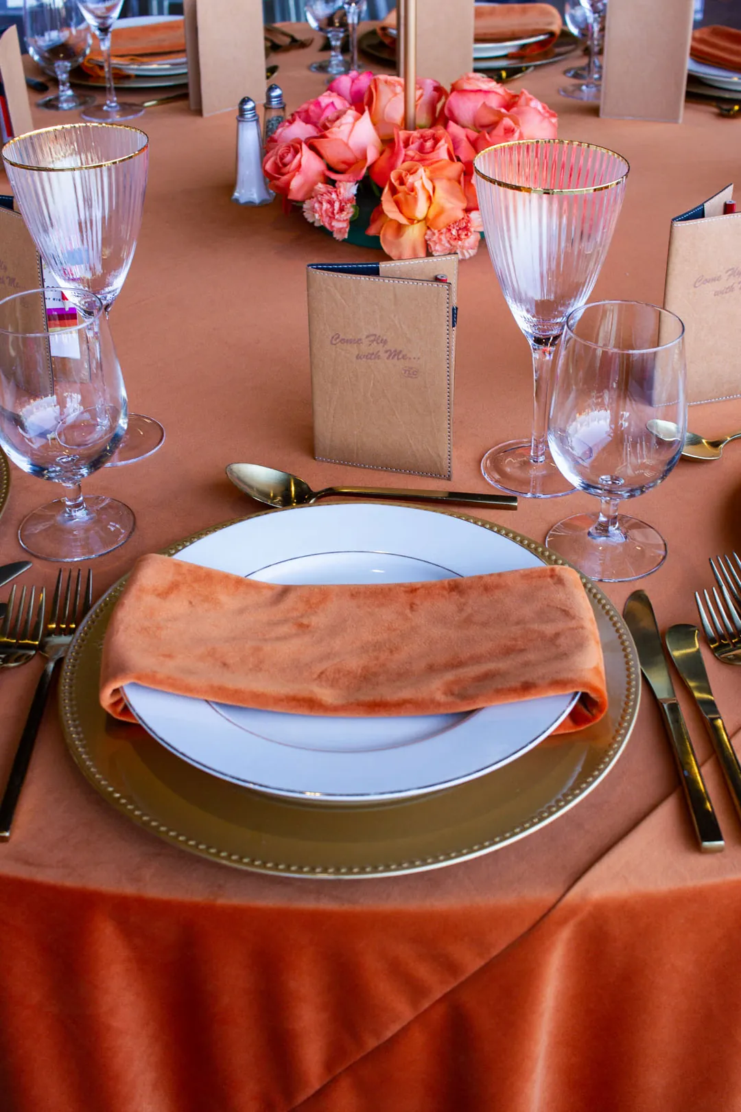 Orange velvet-draped place setting with gold charger, folded velvet napkin and peach roses for the gala dinner