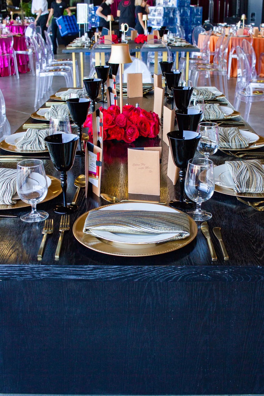 Black draped table with gold chargers, black goblets and red rose centerpiece set for dinner at The Executive Hangar