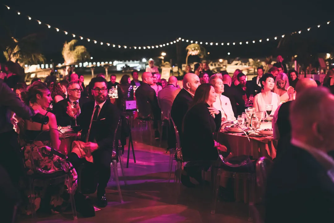 Gala guests seated at dinner tables under string lights on the tarmac at The Executive Hangar at night